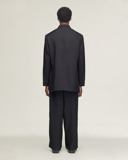 A model viewed from the back wearing a black long-sleeve blazer and matching wide-leg trousers against a plain light gray studio background.